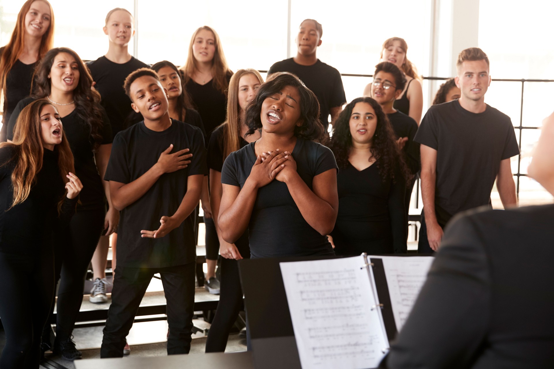 Estudiantes masculinos y femeninos cantando en coro con profesor en la escuela de artes escénicas